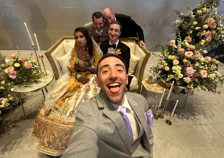 Jacob taking a selfie with his brother and sister-in-law in the background in wedding attire
